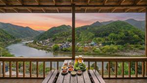 a table with plates of food on a balcony with a river at gapyeong newcastle pension in Gapyeong