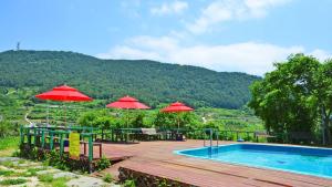 a swimming pool with red umbrellas and a table and chairs at Tongyoung Macaio Pension in Tongyeong