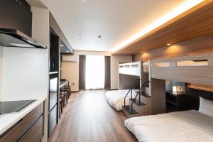 a room with two bunk beds and a desk and a kitchen at ReLA Kashiwa Eki Mae in Kashiwa