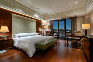 a bedroom with a large bed with a desk and a balcony at Sheraton Changbaishan Resort in Fusong +46 photos