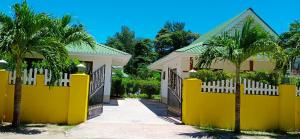a yellow fence in front of a house with palm trees at Le Surmer Self Catering Chalets in La Digue
