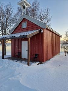 a red barn with two chairs in the snow at The Old Cottage in Harstad