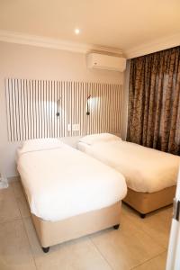 two beds in a hotel room with white sheets at Zar Hotel in Amanzimtoti