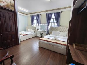 a bedroom with two beds and a table and two windows at The Cloud Hotel in Da Lat