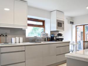 a white kitchen with white cabinets and a window at Mill House Barn in Warmingham