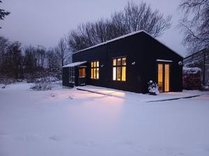 a black house with lights on in the snow at Agerdal - dejligt hus midt i mark og have in Nykøbing Mors
