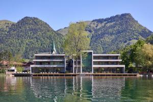 a building on the water with mountains in the background at Das Lakeside - Move&Relax in Walchsee