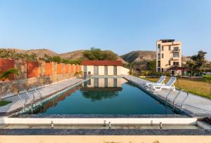 a pool of water with two chairs in front of a building at Shivaangan By Soma Estates in Udaipur