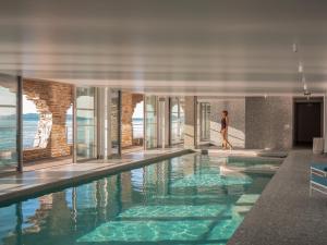 a person walking by a swimming pool in a building at Hôtel Les Roches - Relais & Châteaux in Le Lavandou