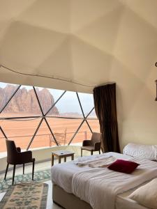 a bedroom with a bed and two chairs and a large window at Golden Stars Luxury Camp Wadi Rum in Wadi Rum