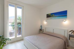 a white bedroom with a bed and a large window at Appartamento Tre Api by ElbaSummer in Procchio