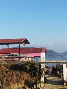 a pink building with a red roof next to the water at Balthali himalaya view point restro in Panaoti