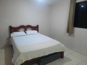 a bedroom with a bed with white sheets and a window at Casa - 1 Suíte e 2 Quartos in Saquarema