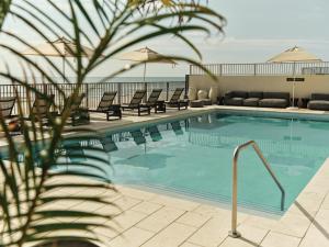 a swimming pool with chaise lounge chairs and the ocean at Ambros Daytona, Trademark Collection by Wyndham in Daytona Beach