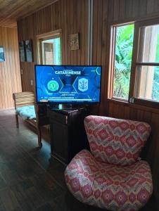 a living room with a flat screen tv and a chair at Sítio em São Bonifácio in Alto Rio Bravo