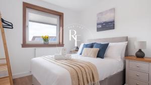 a bedroom with a white bed with blue pillows and a window at The Den at Braehead in Cruden Bay