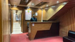 a man standing behind a counter in a room with a staircase at Hotel Priyatama Residential in Dhaka