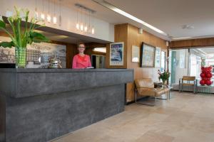 una mujer de pie detrás de un mostrador en el vestíbulo en Hotel Aguado, en Dieppe