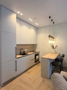 eine Küche mit weißen Schränken, einer Spüle und einem Tisch in der Unterkunft Pine Forest Residence in Melnragė