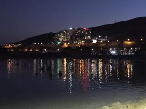 a city lights are reflecting in the water at night at Rose Dead Sea Neve Zohar in Neve Zohar