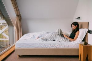 a woman sitting on a bed reading a book at Czas na Las in Żarnowska +69 photos