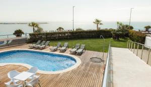 a swimming pool with chairs and the ocean in the background at Hotel Flamingo in L'Ampolla