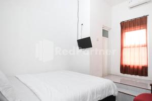 a white bedroom with a bed and a window at Katup Guest House Syariah Mitra RedDoorz in Yogyakarta