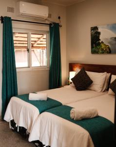 a bedroom with two beds with green curtains and a window at Jollyboys Backpackers and Camp in Livingstone