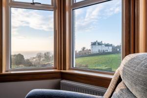 a bedroom with three windows with a view of a house at Avoncliffe in Crail