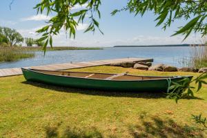 a green boat sitting on the grass next to a dock at Ferienhaus Peeneblick - exklusives Traumhaus in Direktlage am Wasser mit Bootssteg und Aussensauna in Rankwitz +38 photos