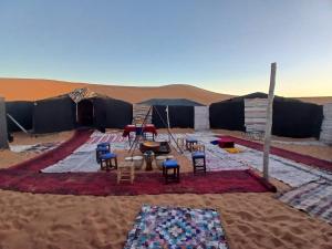a tent in the desert with chairs and tables at Merzouga Camp and Hostel in Merzouga