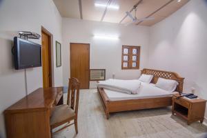 a bedroom with a bed and a desk and a television at Hotel Bhakti Dhama in Vrindāvan