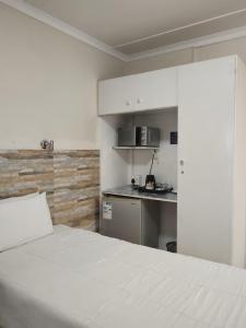 a bedroom with a white bed and a kitchen at Concord Christian Guesthouse in Durban
