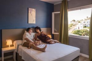 two people sitting on a bed in a bedroom at Aparthotel Nelva Resort in Cala en Porter +60 photos