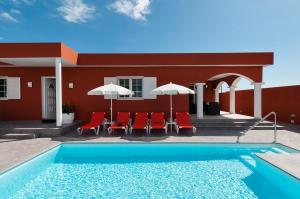 a pool in front of a red building with chairs and umbrellas at Sol y Mar El Salobre in Maspalomas