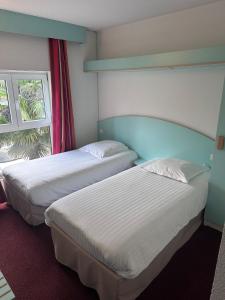 two beds in a hotel room with a window at Agape Hotel Niort- Bessines in Bessines