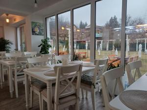 a restaurant with white tables and chairs and windows at Pensiunea CARLA in Sărata-Monteoru