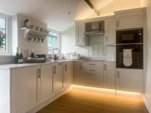 a white kitchen with white cabinets and black appliances at Garth Cottage in Keswick +14 photos
