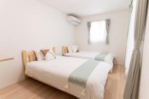 two beds in a room with white walls and wooden floors at Naha Airport NewVilla 4 bedrooms, 2 modern bathrooms, 3 FREE parking in Itoman