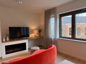 a living room with a television and a red chair at L'Excelsior Suites in Brasschaat