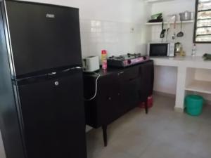 a kitchen with a black refrigerator and a counter at Les Datchi Cottages in Diani Beach +6 photos