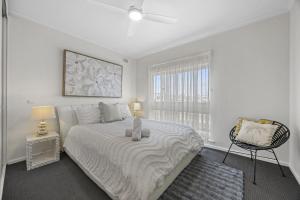 a white bedroom with a large bed and a chair at Sunset Seas in West Beach in West Beach