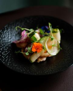 a black plate with a salad with a flower on it at Logis Hotel-restaurant Les Glycines in Arles-sur-Tech