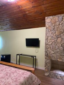 a bedroom with a tv and a stone wall at Pousada Sitio Roda D'Água Mairinque in Mairinque