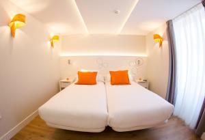 a white bed with two orange pillows in a room at Hostal riMboMbin in Burgos