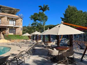 a patio with chairs and an umbrella next to a pool at Pousada Camping Quedasdagua in Barra do Rio Abaixo