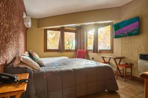 a bedroom with a bed and a desk and two windows at Hotel Xumec Mendoza Centro in Mendoza