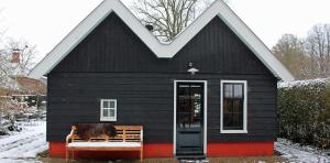 a black house with a cow sitting on a bench at Het Verborgen Jagershuisje in Wedde