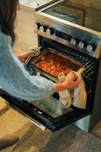 a woman taking a dish out of an oven at Domek Pod Sosnami in Bronków