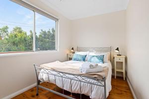 a white bedroom with a bed and a window at Sunbeam Cottage on the Lake in Toukley